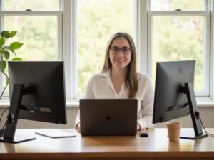 A woman sitting at her desk with two monitors.