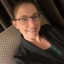 Smiling person wearing glasses and black jacket.