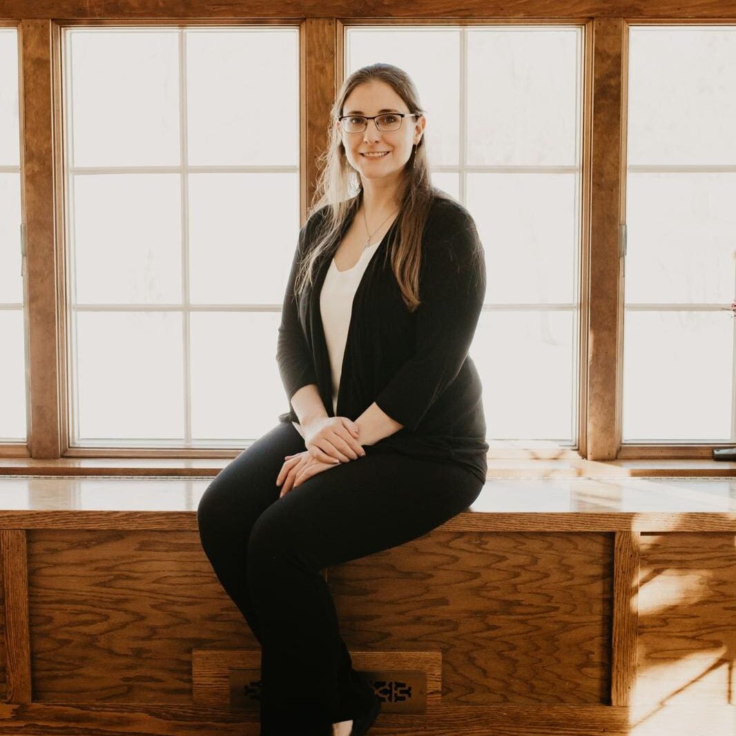 Woman sitting on wooden bench by window.